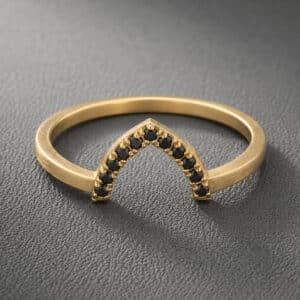 Black diamond V curved guard band in 14K yellow gold featuring eleven micropavé black diamonds in a minimalist chevron contour wedding band design.