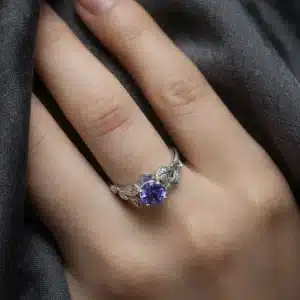 Botanical engagement ring with a round tanzanite center stone, sculpted leaves, hand engraving, and milgrain edging in 14K white gold.