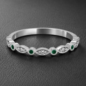 Delicate 14K yellow gold wedding band featuring alternating bezel-set green emeralds and pavé-set diamonds with milgrain edges.