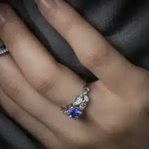 Hand-engraved white gold engagement ring with a 1ct round tanzanite center stone and detailed leaf-shaped accents.