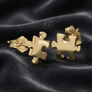 Solid gold puzzle piece earrings with modern minimalist style and polished finish photographed on dark fabric background