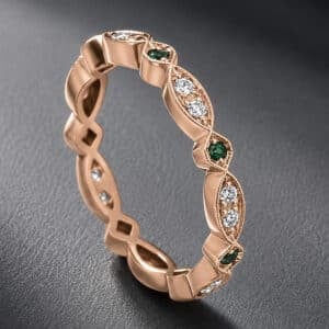 Modern hexagon eternity band featuring green emeralds and diamonds in a pavé setting with hand milgrain edges and a rose gold finish.