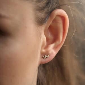 Woman wearing olive branch climber earrings in 14K yellow gold with diamond accents by OroSpot.