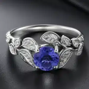Nature-inspired tanzanite engagement ring featuring a round tanzanite center stone, hand-carved leaf details, milgrain edges, and solid 14K white gold.
