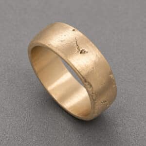 Close up of textured gold men’s wedding band showing raw surface scratches and matte finish OroSpot