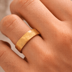 textured yellow gold men's wedding band worn on a man's middle finger with rustic scratched finish handcrafted by orospot