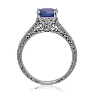 Cushion-cut antique sapphire engagement ring with vintage hand engraving, peekaboo diamonds, and polished rhodium finish in 14K white gold.