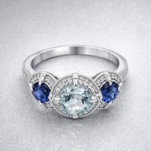 Aquamarine sapphire engagement ring with round center stone, blue sapphire side stones, diamond halos, and white gold band