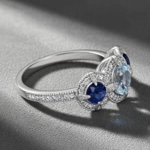 Modern aquamarine sapphire engagement ring with round center stone, blue sapphire side stones, diamond halos, and white gold band by OroSpot.