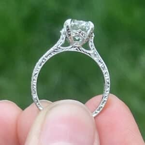 Hand engraved vintage engagement ring with cathedral setting and milgrain detail shown in side profile held between fingers