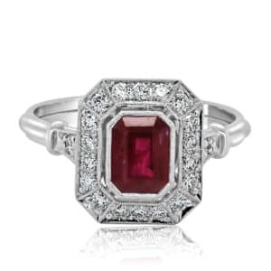 Close-up of emerald cut ruby ring with diamond halo, filigree gallery, and vintage Art Deco hand engraving.