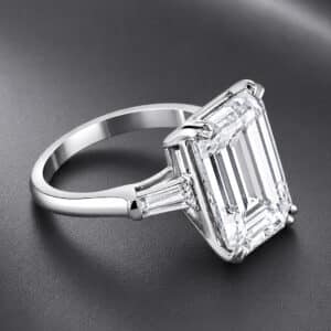 Angled view of a three-stone emerald-cut diamond engagement ring with tapered baguette side diamonds.