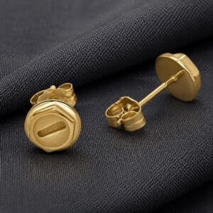 Small gold screw stud earrings with plus and minus details photographed on dark luxury fabric background.