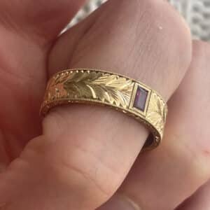 Antique ruby men’s wedding ring in solid 18K gold featuring a flush-set baguette-cut ruby, hand-engraved vintage scrollwork, milgrain edges, and 6mm comfort fit band.