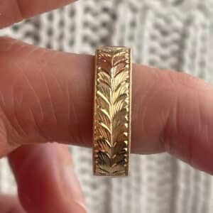 Vintage-inspired men’s wedding band in 18K gold with baguette ruby center, hand-engraved detailing, milgrain edges, and polished 6mm comfort fit profile.