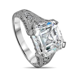 Three-stone diamond ring with Asscher cut center and trillion side diamonds, featuring hand engraving, pavé accents, and vintage Art Deco styling.