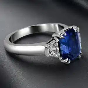 Three-stone engagement ring with a royal blue lab-grown sapphire center and trapezoid diamond side stones in a sleek modern setting.