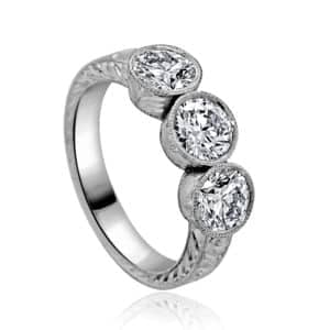 hand-held view of a vintage three-stone bezel ring with lab-grown diamonds, low profile, hand-engraved sides — OroSpot