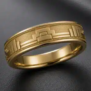 3/4 angle view of a 6mm New York Art Deco men's wedding band featuring an architectural keystone motif, geometric skyline-inspired details, fine texture, and milgrain borders in yellow gold.